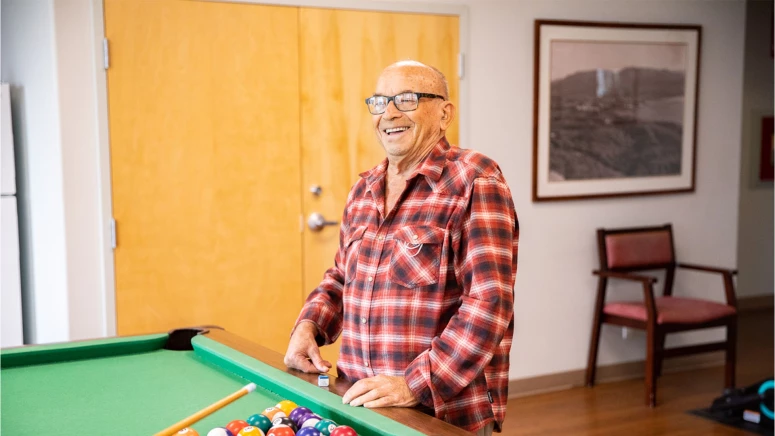 An elderly man playing 8 ball pool at penticton's residence